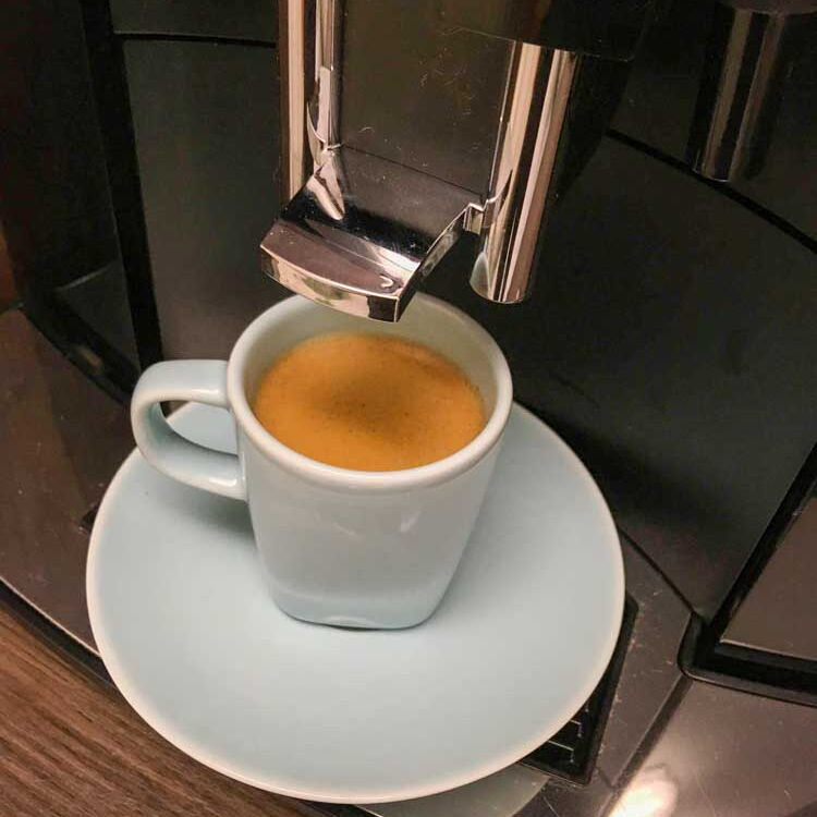 Eine Tasse leckerer, frisch gebrühter Espresso steht unter der Espressomaschine.
