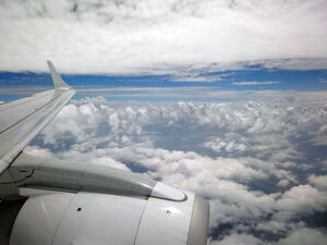 Der Blick aus einem Flugzeugfenster auf die Tragfläche mit Triebwerk und einen wolkenreichen von der Sonne beschienenen Himmel. Die Flugangst loswerden und wieder entspannt fliegen.