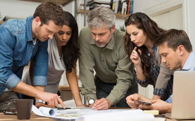 Ein Team steht über einem Tisch mit Unterlagen und berät sich