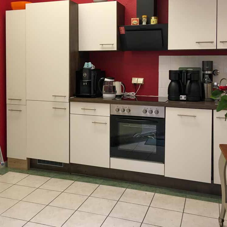 Die vollständig eingerichtete Küche in der Coachingpraxis. mit Espresso-Maschine, Herd, Spülmaschine. Die Wände sind rot gestrichen.