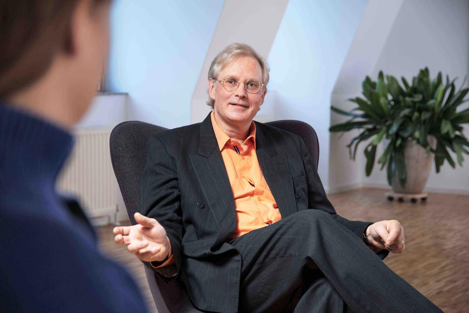 Reiner Müller ist Angsttherapeut und Coach und spezialisiert auf die Unterstützung bei Präsentationsangst. Auf diesem Bild ist er sitzend zu sehen, wie er etwas erklärt.