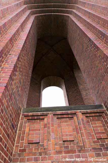 Ein aus Ziegelsteinen gemauerter Turm. Durch ein großes Fenster fällt Licht.